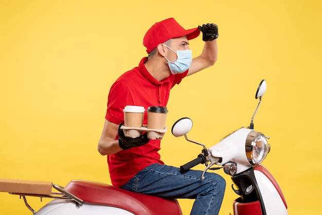 Männlicher Kurier der Vorderansicht in Uniform und Maske mit Kaffee auf gelbem Farbjob-Covid-Work-Food-Service-Virus