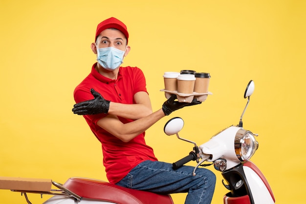 Männlicher Kurier der Vorderansicht in Uniform und Maske mit Kaffee auf gelbem Food-Service-Job Covid-Virus-Arbeitsfarben-Pandemie