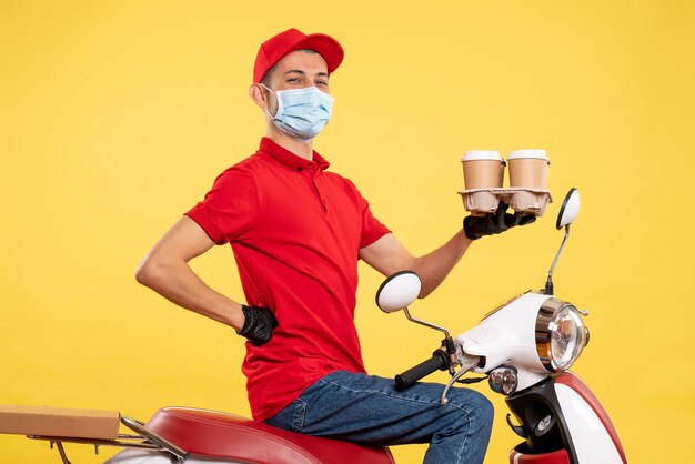 Männlicher Kurier der Vorderansicht in Uniform und Maske mit Kaffee auf gelber Dienstjobpandemie-Covid-Virus-Arbeitsfarbe