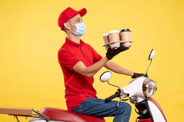 Männlicher kurier der vorderansicht in uniform und maske mit kaffee auf gelber food-service-job-pandemie-covid-virus-arbeitsfarbe