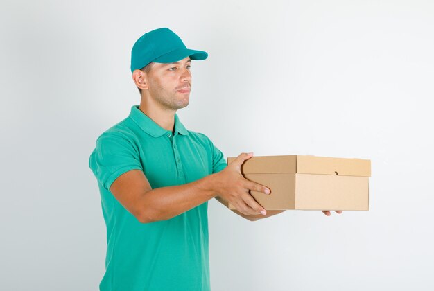 Männlicher Kurier im grünen T-Shirt mit Kappe, die Karton liefert