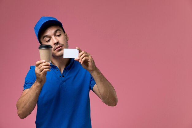 männlicher Kurier in blauer Uniform, die Kaffee und Karte auf rosa, Arbeiteruniform-Dienstlieferung hält