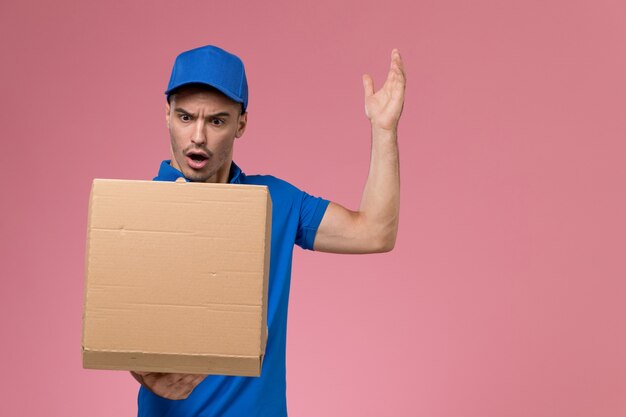 männlicher Kurier in blauer Uniform, die Lieferbox des Lebensmittels hält, das es auf rosa, einheitlicher Servicezustellung öffnet