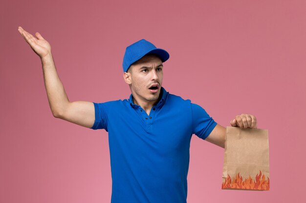 männlicher Kurier in blauer Uniform, die Liefernahrungsmittelpaket auf rosa, Dienstarbeiteruniformdienstlieferung hält