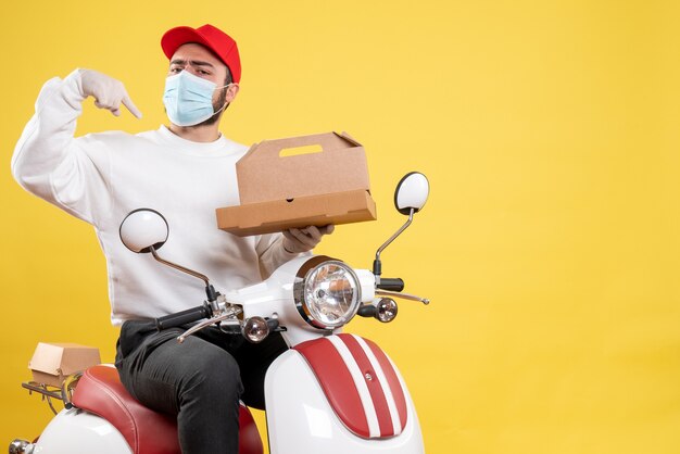 männlicher Kurier in Maske auf Fahrrad hält Lebensmittelbox auf Gelb