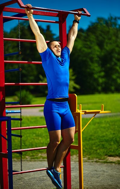 Männlicher Mann hübschen gesunden glücklichen srtong Athleten, der am Stadtpark - Eignungskonzepte an einem schönen Sommertag auf horizontaler Stange trainiert