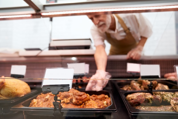 Männlicher Metzger, der rohes Fleisch aus der Theke nimmt.