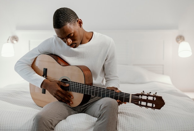 Männlicher Musiker auf dem Bett, das Gitarre spielt