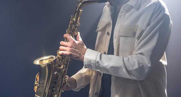 Männlicher Musiker auf der Bühne spielt das Saxophon dunkel vor Rauch