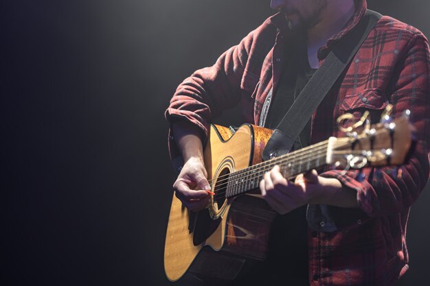 Männlicher Musiker, der akustische Gitarre in einem dunklen Raumkopierraum spielt.