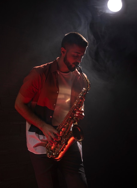 Kostenloses Foto männlicher musiker, der das saxophon im rampenlicht spielt