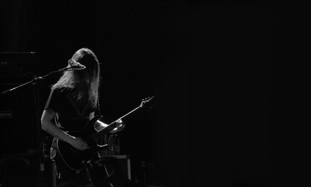 Kostenloses Foto männlicher musiker, der gitarre auf einer bühne nahe dem mikrofon in schwarzweiss spielt