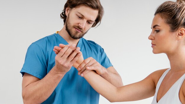 Männlicher osteopathischer Therapeut, der das Handgelenk des weiblichen Patienten überprüft