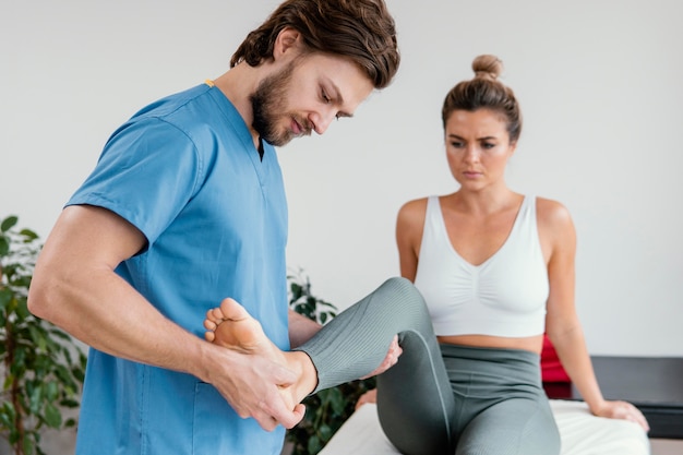 Männlicher osteopathischer Therapeut, der die Beinbewegung der Patientin überprüft