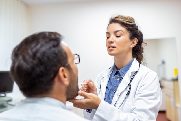 Männlicher Patient öffnet den Mund für den Arzt, um seinen Hals zu betrachten Ärztin untersucht Halsschmerzen des Patienten in der Klinik Hals-Nasen-Ohrenarzt untersucht Halsschmerzen des Patienten