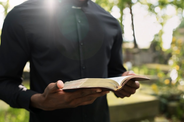 Männlicher Priester, der am Grab mit trauernder Familie aus der Bibel liest