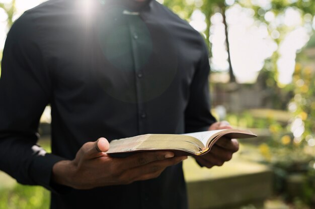 Männlicher Priester, der am Grab mit trauernder Familie aus der Bibel liest