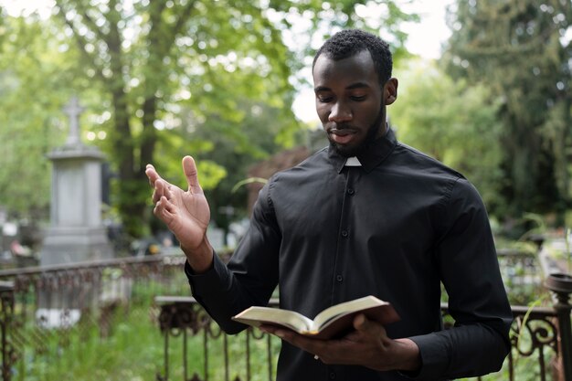 Männlicher Priester, der die Bibel auf dem Kirchhof liest