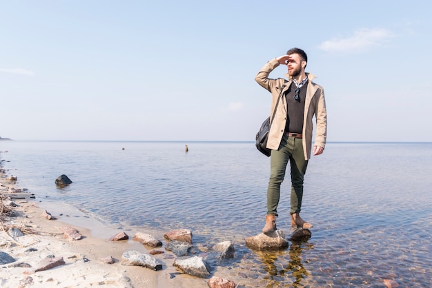 Männlicher Reisender, der nahe dem See abschirmt seine Augen steht