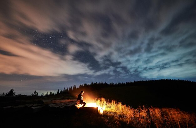 Männlicher Reisender, der unter schönem Nachthimmel mit Sternen sitzt