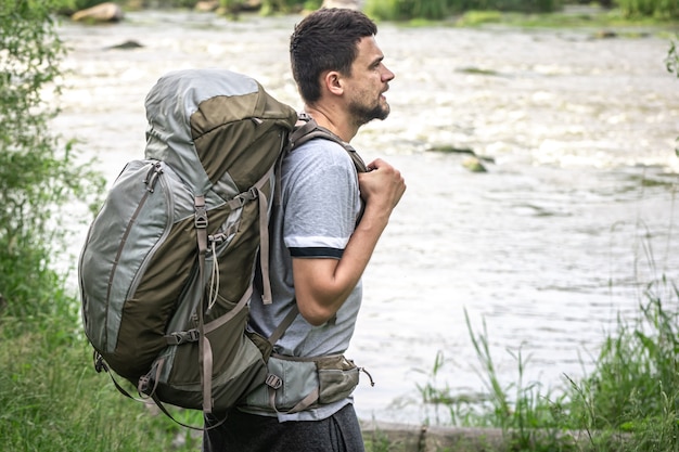 Männlicher Reisender mit einem großen Wanderrucksack in der Nähe des Flusses.