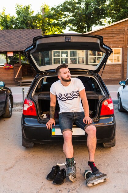 Männlicher Rollerskater, der auf Stamm eines Autos sitzt