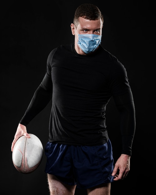 Kostenloses Foto männlicher rugbyspieler mit der medizinischen maske, die ball hält