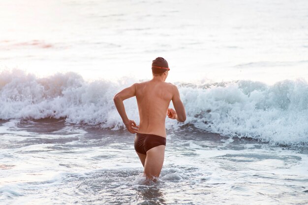 Männlicher Schwimmer mit Schutzbrille und Mütze, die in den Ozean gehen