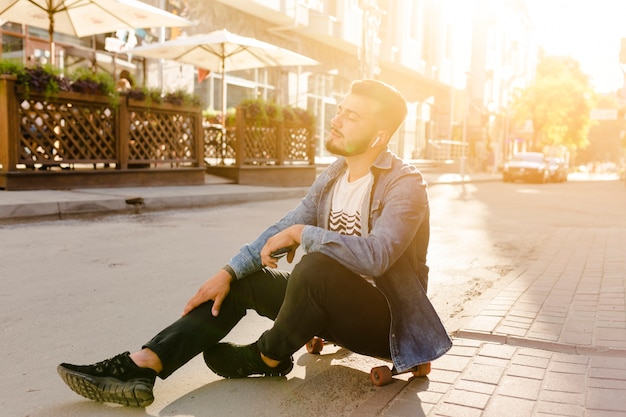Kostenloses Foto männlicher skateboardfahrer, der auf dem skateboard hört musik sitzt