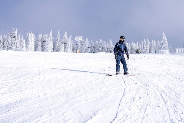 Männlicher Snowboarder fährt den Hang hinunter mit einer wunderschönen Winterlandschaft im Hintergrund