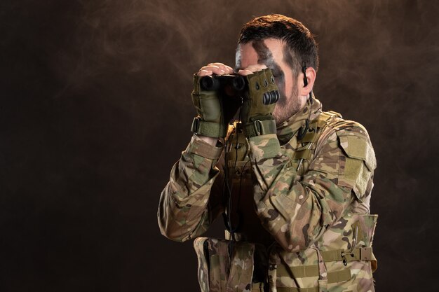 Männlicher Soldat in Militäruniform mit Fernglas an der dunklen Wand