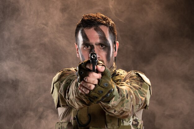 Männlicher Soldat in Tarnung, der mit einer Waffe auf die rauchige dunkle Wand zielt