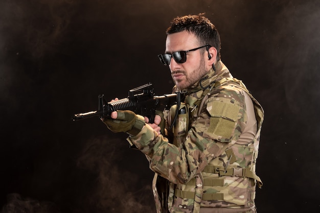 Männlicher Soldat in Tarnung mit Maschinengewehr an dunkler Wand