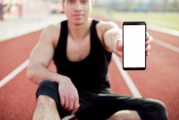 Männlicher Sportler, der auf der Rennstrecke zeigt Handyschirm sitzt