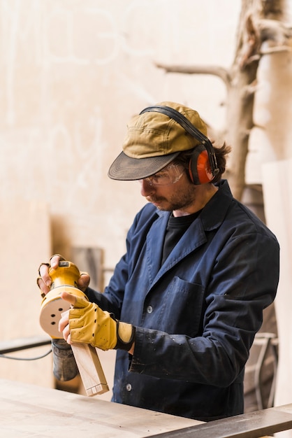 Kostenloses Foto männlicher tischler bearbeitet den block mit einem zufälligen orbitsandschleifer in der werkstatt