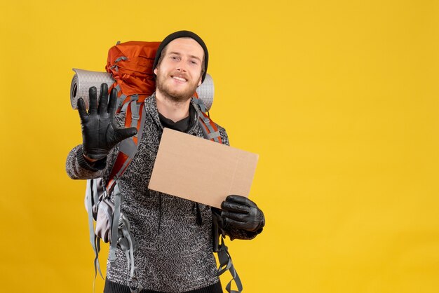 männlicher Tramper mit Lederhandschuhen und Rucksack mit leerem Karton, der Stoppschild macht