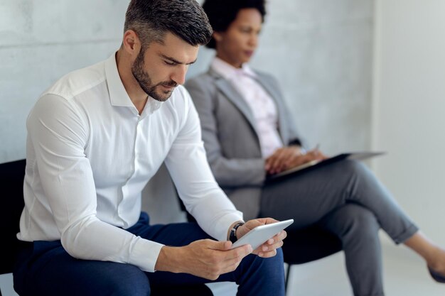 Männlicher Unternehmer, der Touchpad verwendet, während er auf ein Vorstellungsgespräch wartet