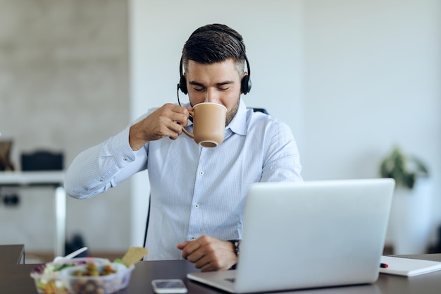 Männlicher Unternehmer genießt den Geschmack von frischem Kaffee, während er im Büro arbeitet