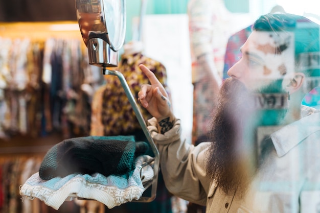 Männlicher Verkäufer, der Gewebegewicht auf Skalen am Kleidungsshop gesehen durch Glas überprüft