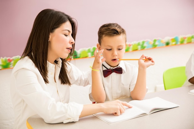 Männlicher Vorschulschüler, der Uniform trägt und Hilfe von seinem Lehrer in einem Klassenzimmer bekommt