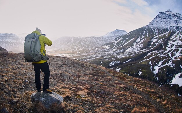 Männlicher Wanderer mit einem Rucksack, der ein Foto der felsigen Berge macht, die im Schnee bedeckt sind