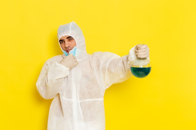 Männlicher wissenschaftlicher arbeiter der vorderansicht im speziellen schutzanzug, der flasche mit blauer lösung auf gelber oberfläche hält