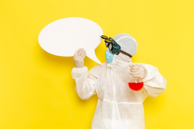 Männlicher wissenschaftlicher Arbeiter der Vorderansicht im speziellen Schutzanzug, der Flasche mit roter Lösung und weißem Zeichen auf gelbem Boden hält