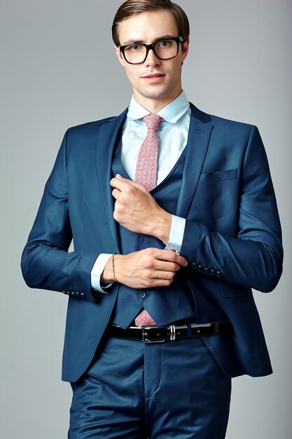 Männliches Modell des jungen eleganten hübschen Geschäftsmannes in der blauen Klage und in den modernen Gläsern, werfend im Studio auf