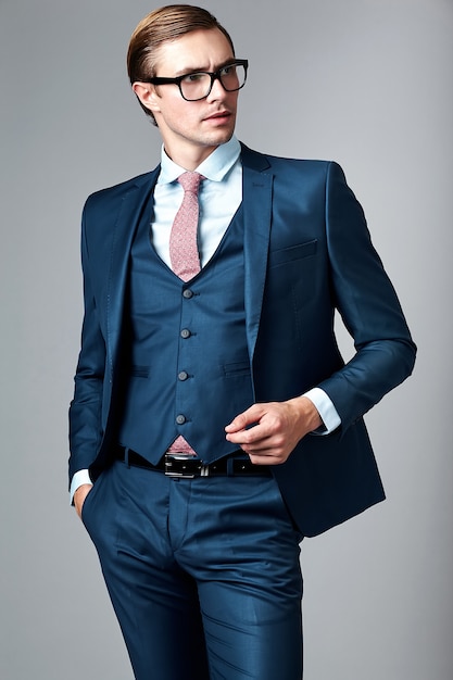 Männliches Modell des jungen eleganten hübschen Geschäftsmannes in der blauen Klage und in den modernen Gläsern, werfend im Studio auf