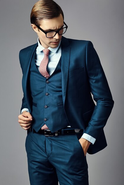 Männliches Modell des jungen eleganten hübschen Geschäftsmannes in einer Klage und in modernen Gläsern, werfend im Studio auf