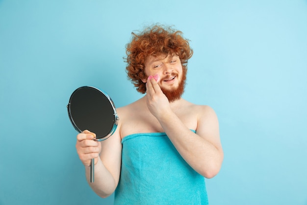 Männliches Modell mit natürlichem rotem Haar, das Feuchtigkeitscreme, Öle auf Gesichtshaut anwendet