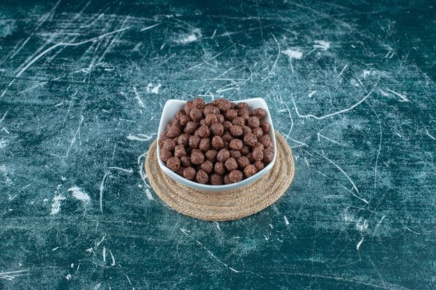 Maisbällchen in einer Schüssel auf einem Untersetzer, auf blauem Hintergrund. Foto in hoher Qualität