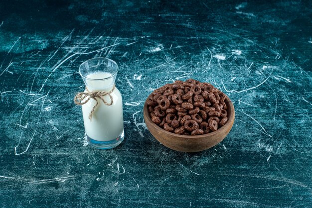 Maisringe in einer Schüssel neben einem Krug Milch auf blauem Hintergrund. Foto in hoher Qualität