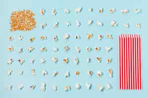 Kostenloses Foto maissamen und reihe von popcorns mit abgestreiftem popcornkasten gegen blauen hintergrund